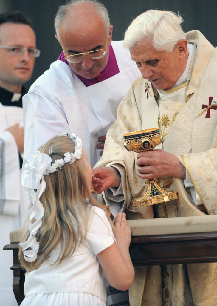 Criança recebendo a Sagrada Comunhão das mãos do Papa Emérito Bento XVI